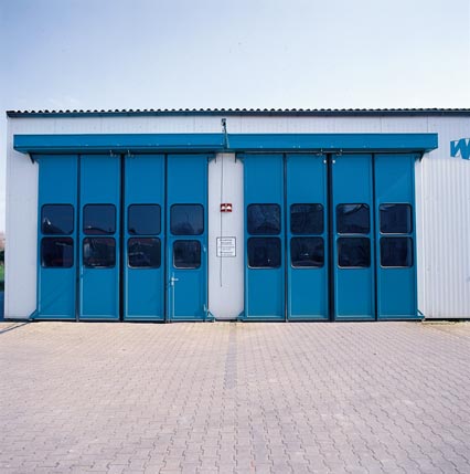 Blaue Stahlfalttore mit Fensterreihe an einem Gebäude